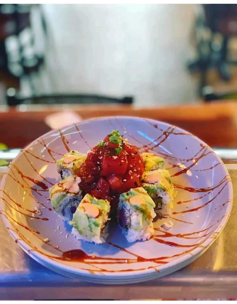 Sushi roll wrapped in sliced avocado and topped with a mound of marinated tuna poke