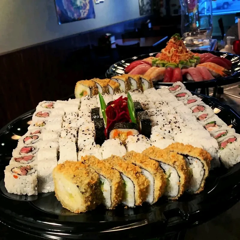 Two large catering sushi platters side by side, rolls in front and nigiri behind