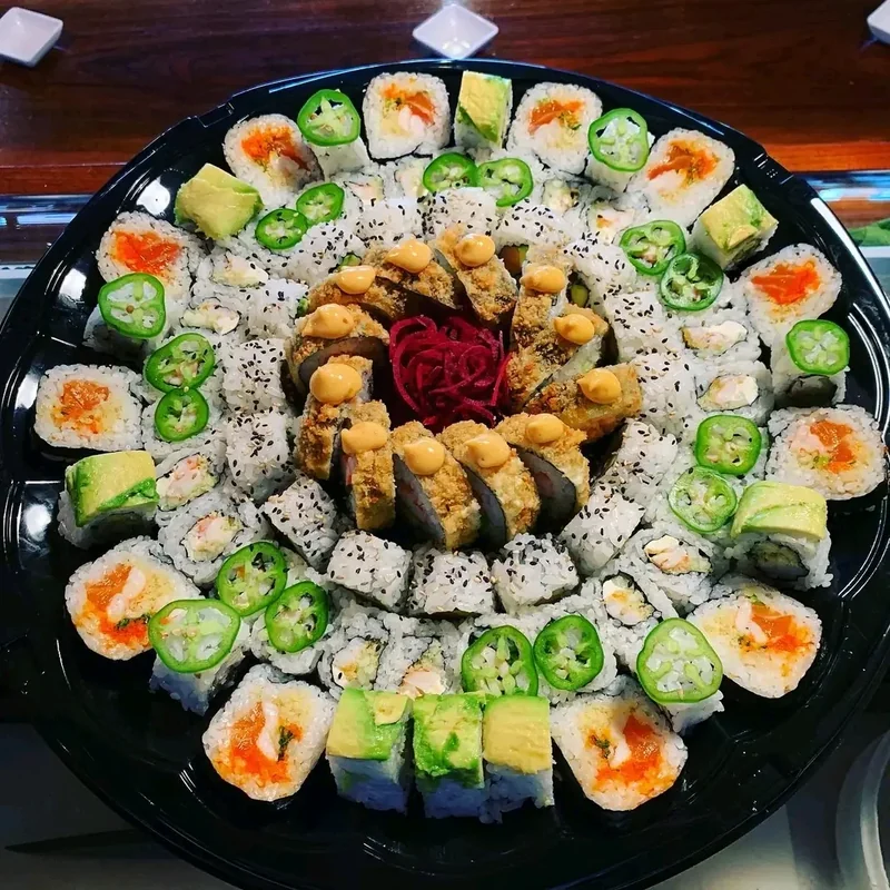 Round catering sushi platter with crispy rolls at the center ringed by jalapeño and avocado topped rolls