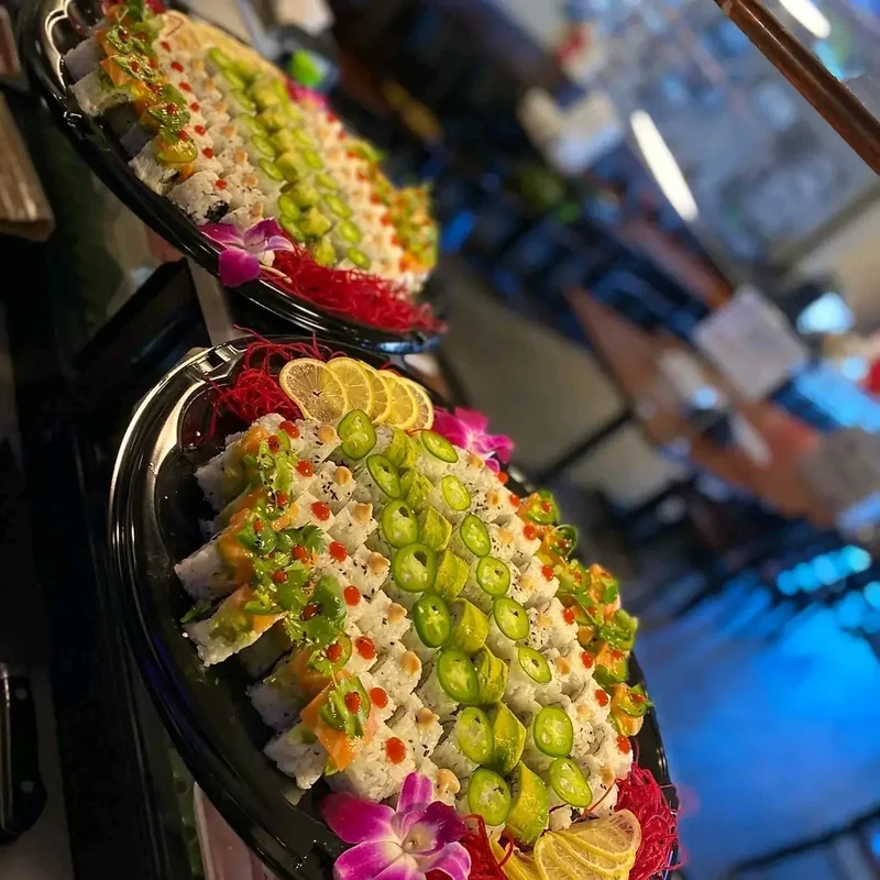 Two long catering sushi trays garnished with herbs, citrus slices and orchids
