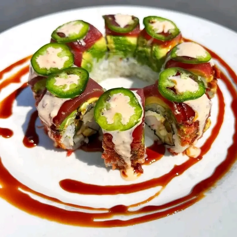 Sushi roll arranged in a circular wreath, topped with fresh jalapeño slices and creamy sauce