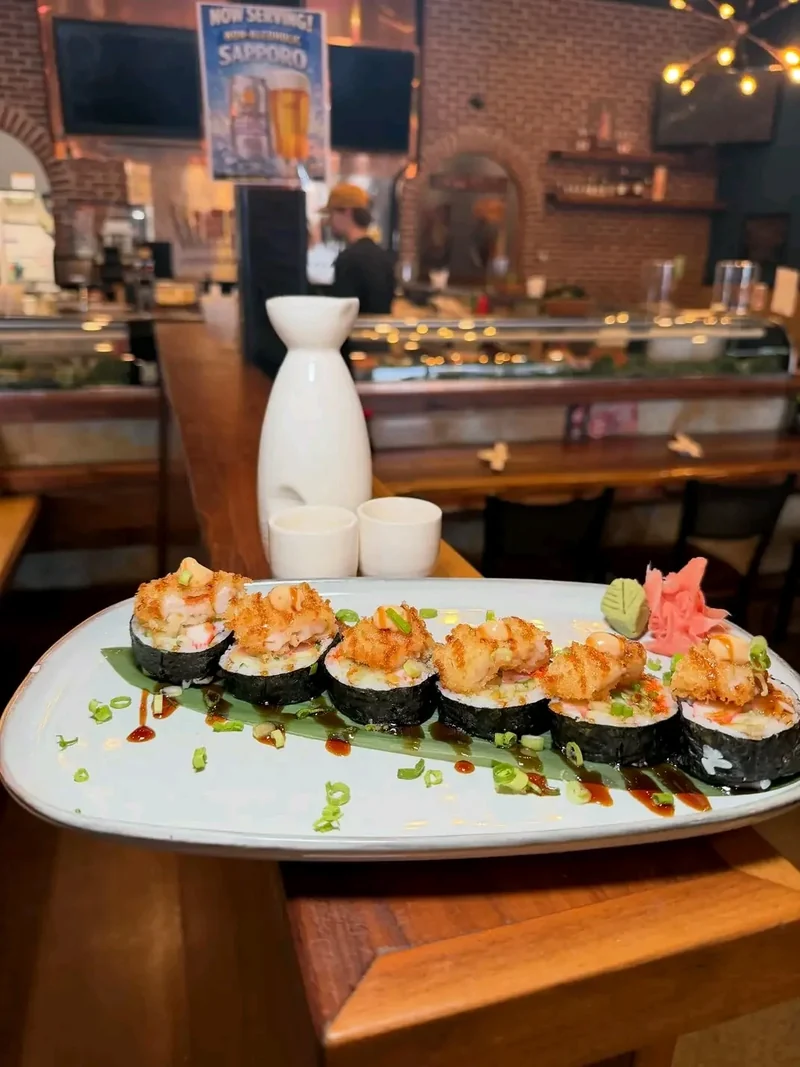 Seafood sushi roll topped with crisp panko, plated on a bamboo leaf with a sake carafe and cups