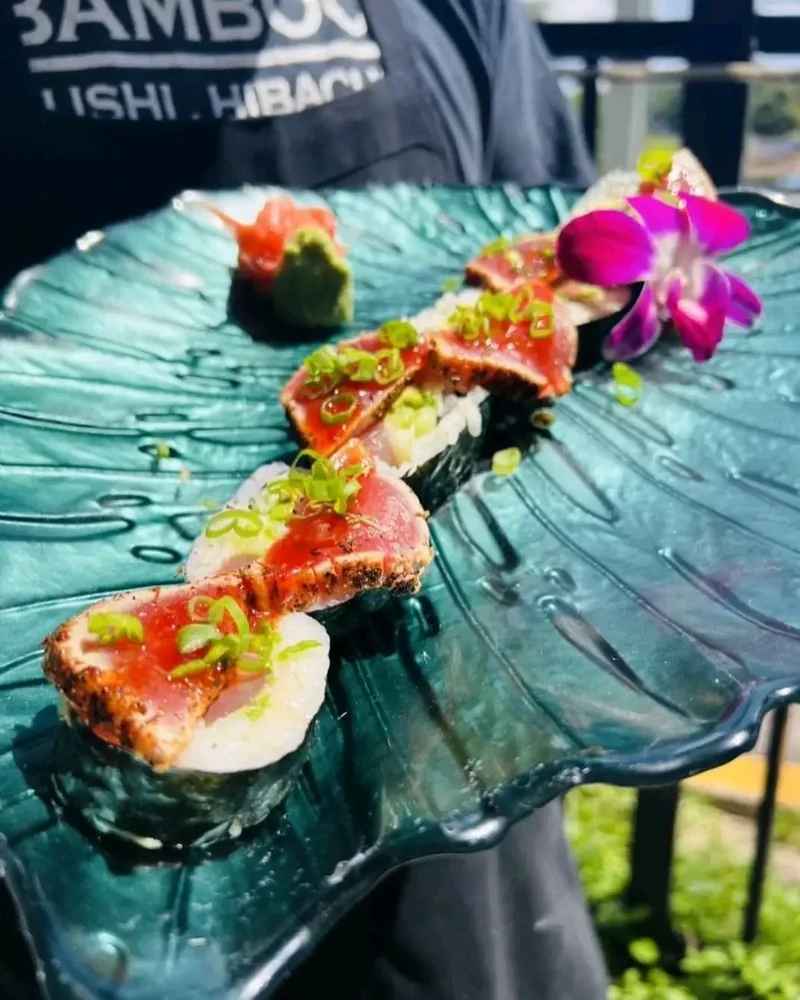 Sushi roll topped with torch-seared tuna, scallions and citrus zest on a green glass plate