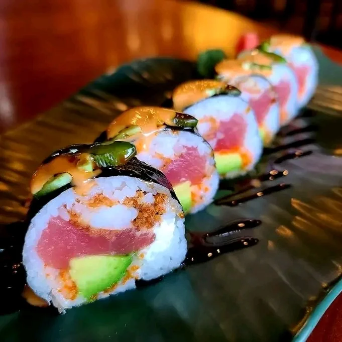 Close-up of a sushi roll topped with tuna, avocado and jalapeño, laced with spicy mayo and eel sauce