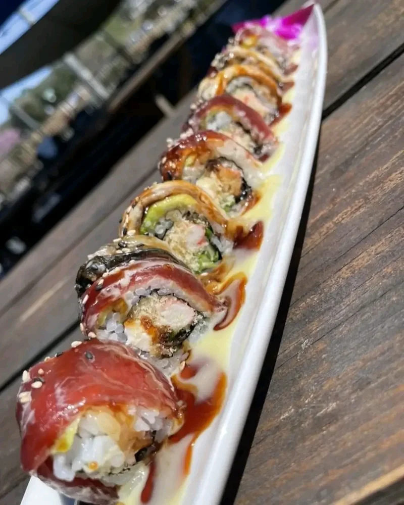 Sushi roll draped in slices of red tuna and finished with eel sauce on a long white plate