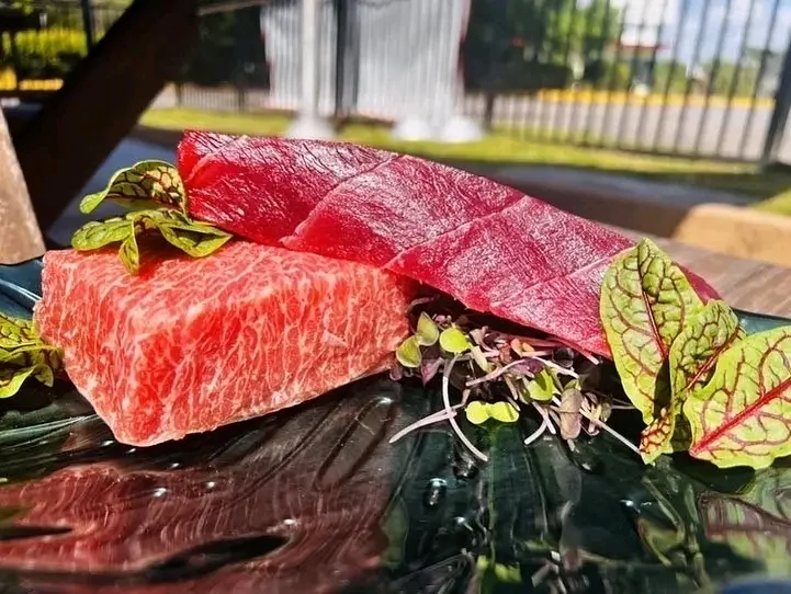 Raw marbled beef block and a block of red tuna arranged with microgreens