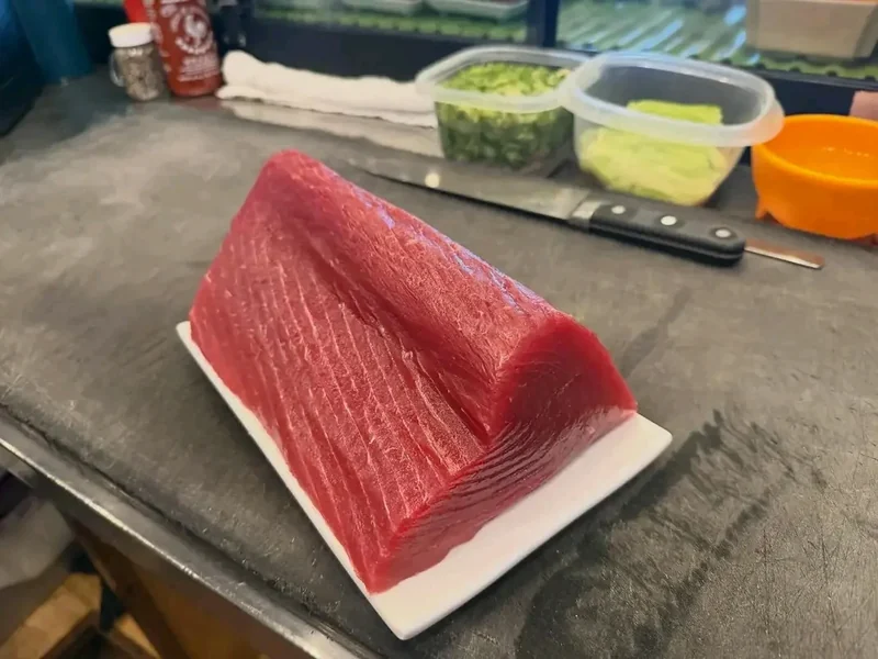 A whole saku block of raw tuna loin on a cutting board in the sushi prep area